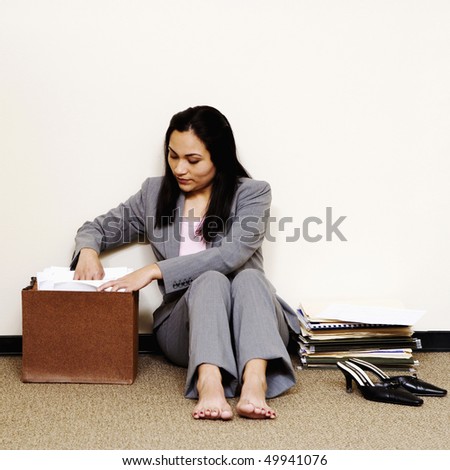 A young businesswoman is sitting on the floor with her shoes off and looking through a file folder. Square shot.