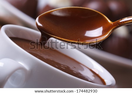 Liquid chocolate dripping from the spoon in a cup closeup horizontal. macro