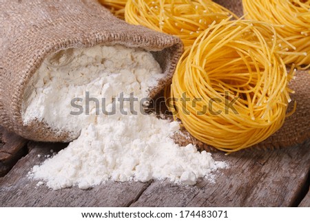 dry pasta in the form of nests and a sack of flour crumble close up on an old wooden table. macro. horizontal
