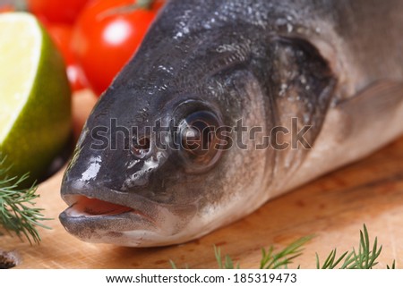 Raw sea bass fish on cutting board with vegetables close-up horizontal. front view