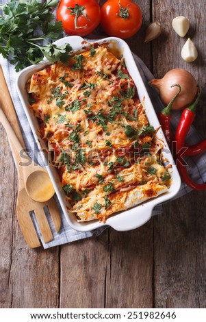 Mexican enchilada in a baking dish with the ingredients on the table. vertical view from above