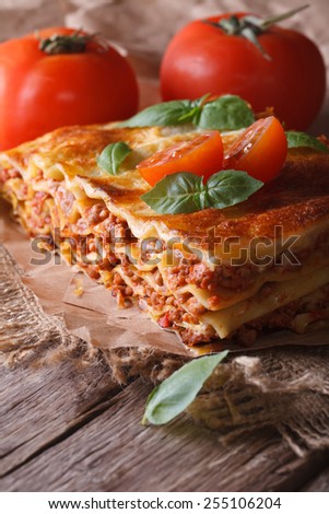 Italian lasagna with basil and tomatoes on an old table, vertical rustic style