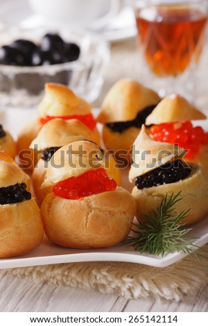 Tasty snack: profiteroles stuffed with red and black caviar on a plate close-up. vertical