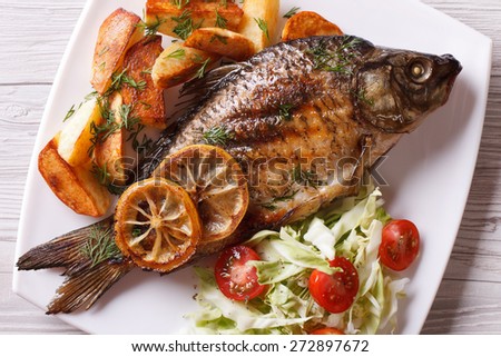 grilled fish with fried potatoes and salad on the plate closeup. horizontal view from above