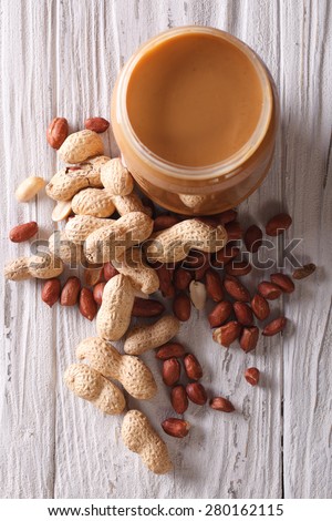 Peanut butter in a glass jar and nuts close up on an old table. vertical top view