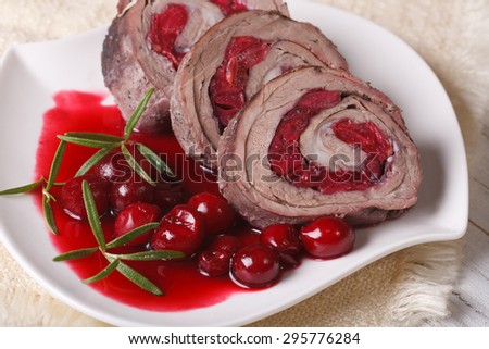 Meat roll filled with cherries and sauce on a plate close-up. horizontal