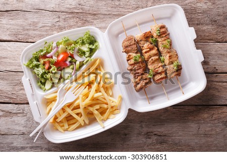 Fast food: kebabs, fries and fresh salad in the tray on the table. horizontal view from above
