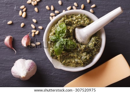 Italian green pesto sauce in a mortar and ingredients close-up on the table. horizontal view from above