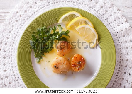 fried scallops with sauce and lemon on a plate close-up. horizontal view from above