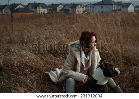 woman sitting with staffordshire terrier in fields behind country town