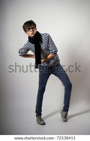 skinny boy model posing on a white background. he wears glasses. dressed in a striped sweater and jeans
