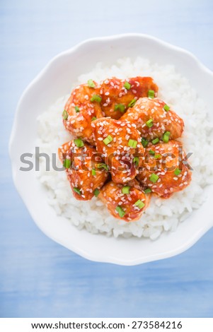 Spicy sweet and sour chicken with sesame and rice on blue wooden background top view. Oriental food.