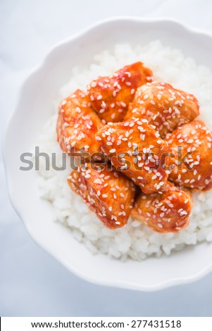 Spicy sweet and sour chicken with sesame and rice on white background top view. Oriental food.