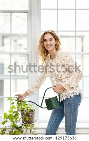 Smiling woman watering green plant at home by window