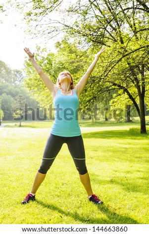 Female fitness instructor stretching at green park in the morning