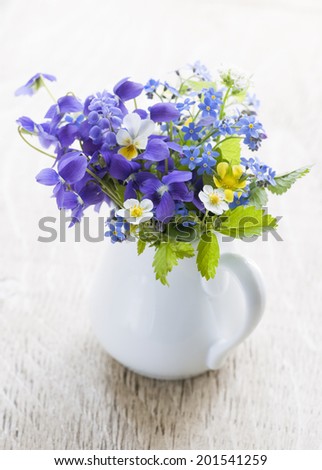 Bouquet of wild flowers in white vase on wood background, studio shot