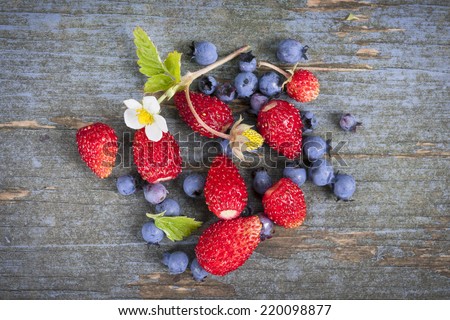 Fresh small wild strawberries and blueberries on old blue wooden background