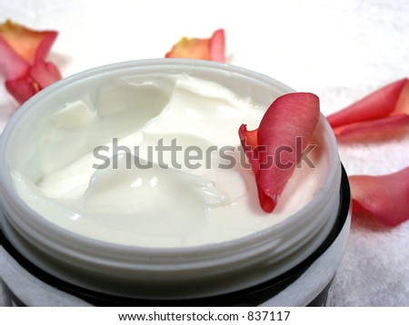 Body cream with rose petals on white towel, closeup
