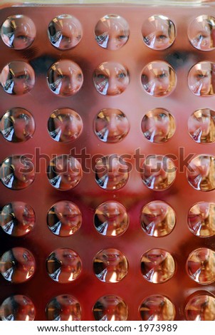 Portrait of a girl photographed through textured glass resulting in many faces on the background of one face; focus on the glass surface
