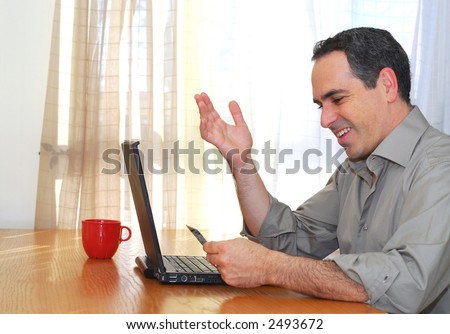 Man sitting at his desk with laptop holding a credit card looking happy