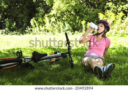Teenage girl resting in a park with a bicycle drinking water