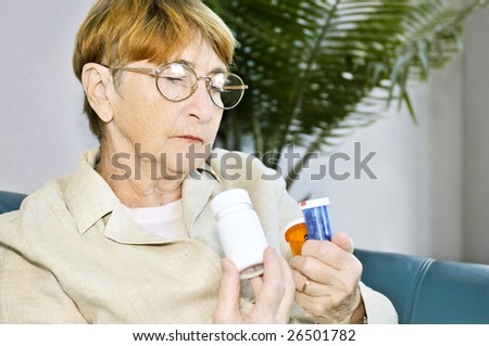 Elderly woman reading warning labels on pill bottles with medication
