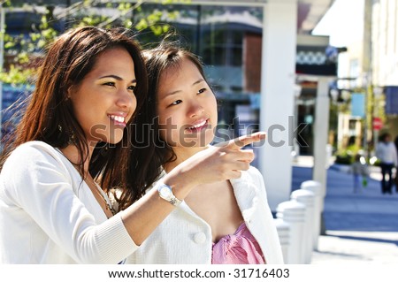 Two young girlfriends at outdoor mall pointing