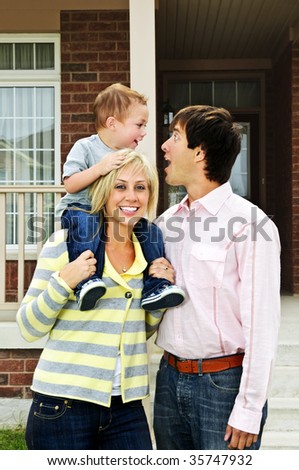 Young happy family standing in front of new home