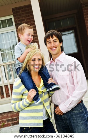 Young happy family standing in front of new home