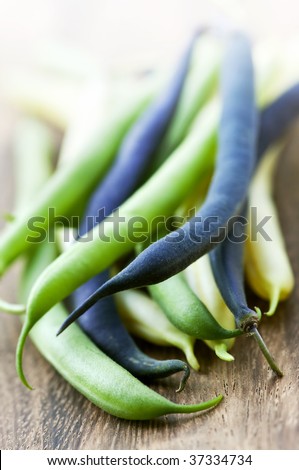 Pile of purple yellow and green string beans on cutting board