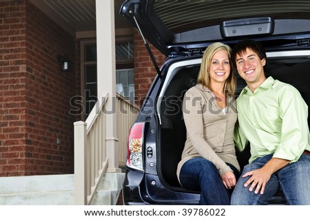 Happy young couple sitting at back of car on driveway