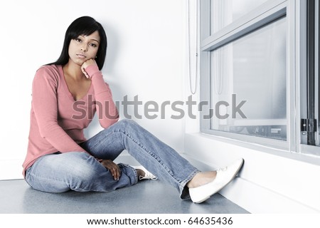 Sad young black woman sitting against wall on floor