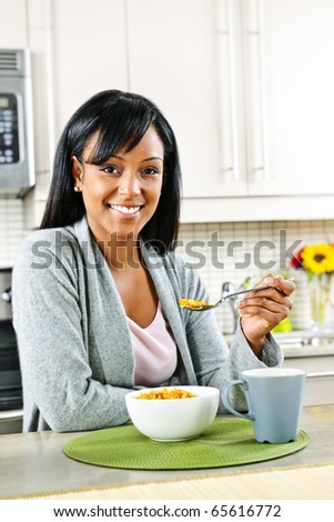 Smiling black woman having breakfast in modern kitchen interior