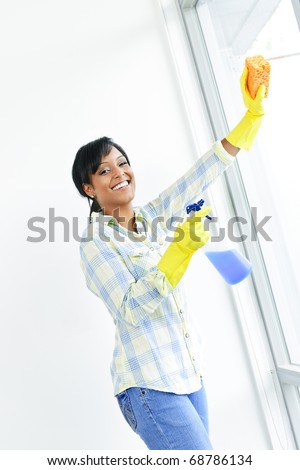 Smiling black woman cleaning windows with glass cleaner