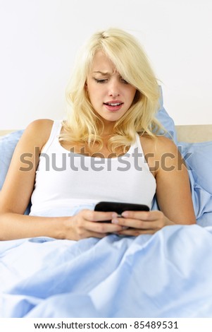 Angry woman reading text message on phone in bed at home