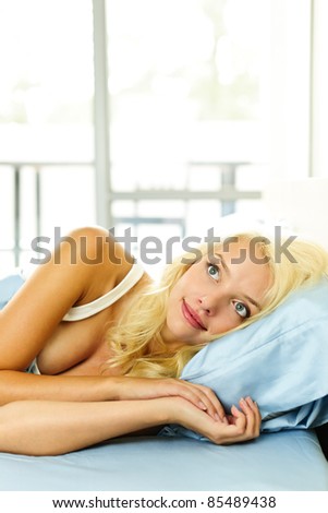 Happy blonde woman laying in bed dreaming and smiling
