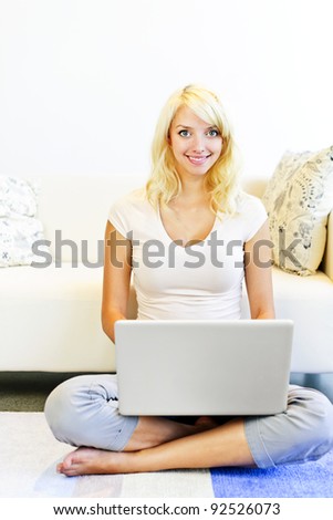 Smiling blonde woman sitting on floor with computer in living room