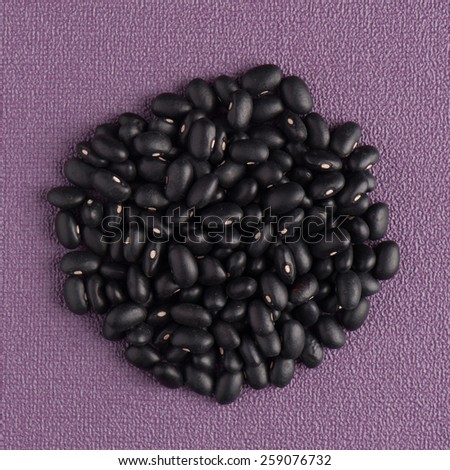 Circle of black beans on purple vinyl background.