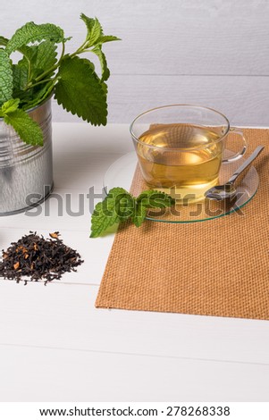 Herbal tea with melissa in a glass cup a green napkin on a white wooden table top.