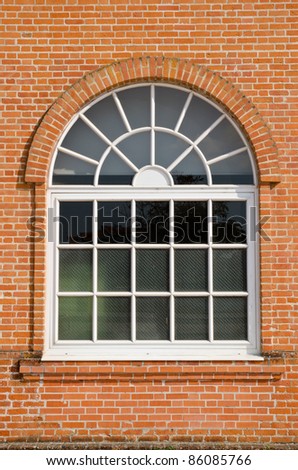 White painted wood arched window in a red brick wall .