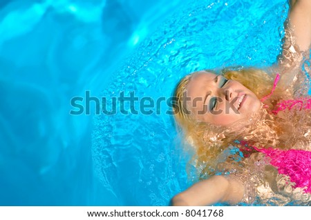 attractive blond female model in pink bikini swims in pool