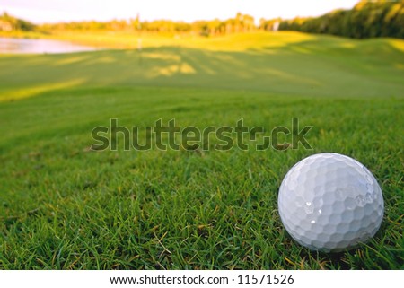 golf ball resting on bunker of lovely golf course with early morning sun hitting the fairway