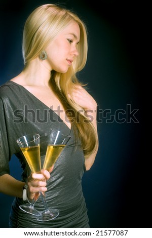 beautiful blond model in party dress holding two flute glasses of bubbling champagne against dark background