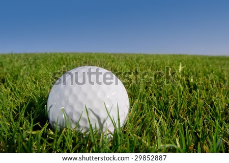 golf ball resting on grassy bunker with blue sky background
