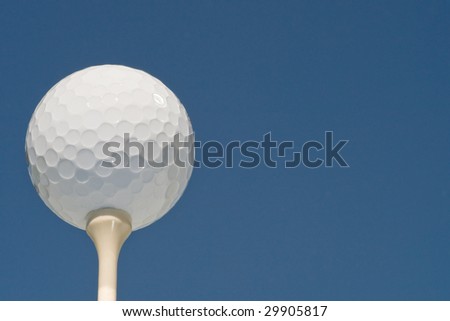 golf ball on tee, low angle, isolated against deep blue sky