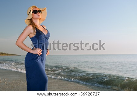 lovely blonde female model in blue dress by atlantic ocean shore with blue sky background