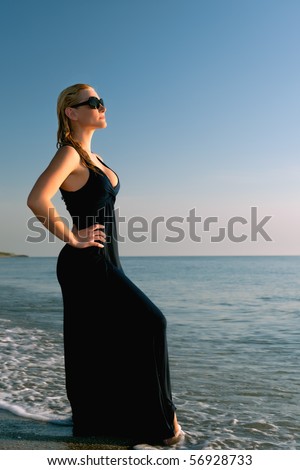 lovely blonde female model in blue dress by atlantic ocean shore with blue sky background