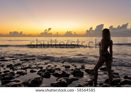 female bikini model silhouetted by sunrise at atlantic ocean beach