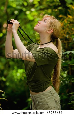 lovely blonde female with binoculars looking around in tropical rainforest