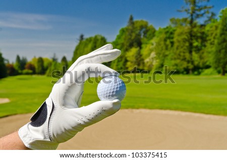 hand showing golf ball over sand bunker at beautiful golf course with blue sky